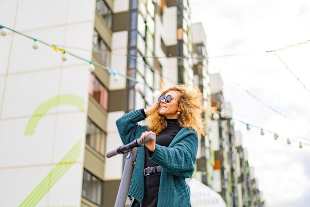 Junge schöne Frau, die einen Elektroroller zur Arbeit reitet, modernes Mädchen, neue Generation, elektrischer Transport, Ökologie, ökologischer Transport, Sonnenuntergang