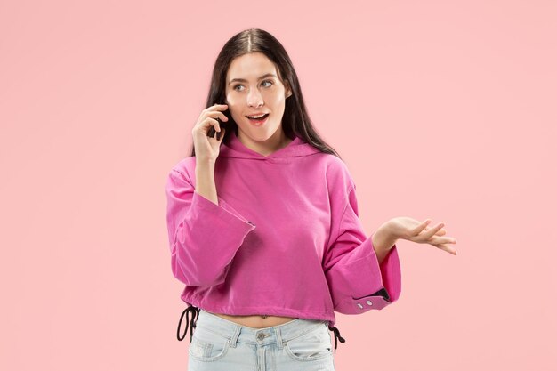 Junge schöne Frau, die Handystudio auf rosa Farbstudiowand verwendet
