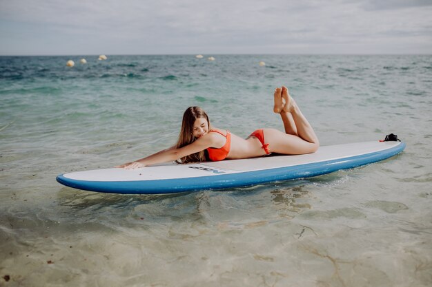 Junge schöne Frau, die im Meer auf einem SUP-Brett entspannt.
