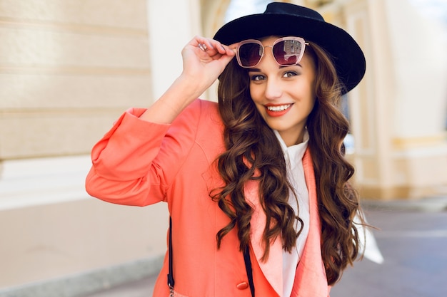 Junge schöne Frau, die in der alten Stadt in den trendigen lässigen Glamourkleidern, rosa Jacke geht. Frühlings- oder Herbstsaison, sonniges Wetter.