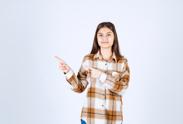 junge schöne frau, die irgendwo auf weiße wand zeigt.