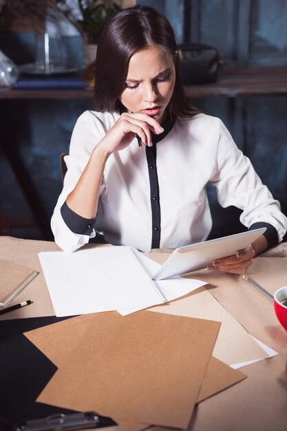 Junge schöne Frau, die mit einer Tasse Kaffee und einem Notebook im Loft-Büro arbeitet