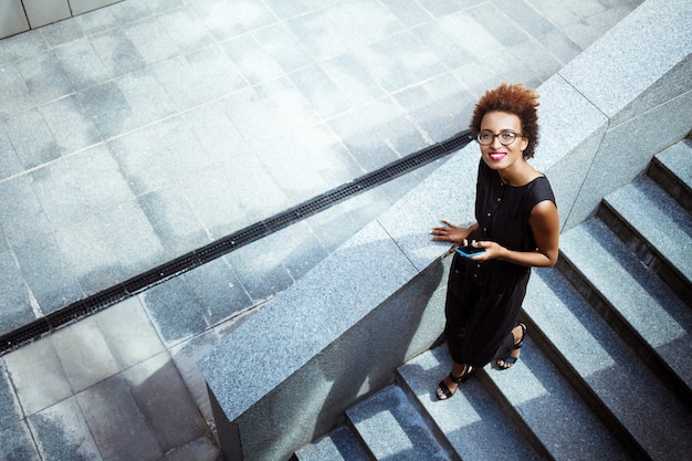 Junge schöne Frau, die Telefon hält, das Treppe hinuntergeht