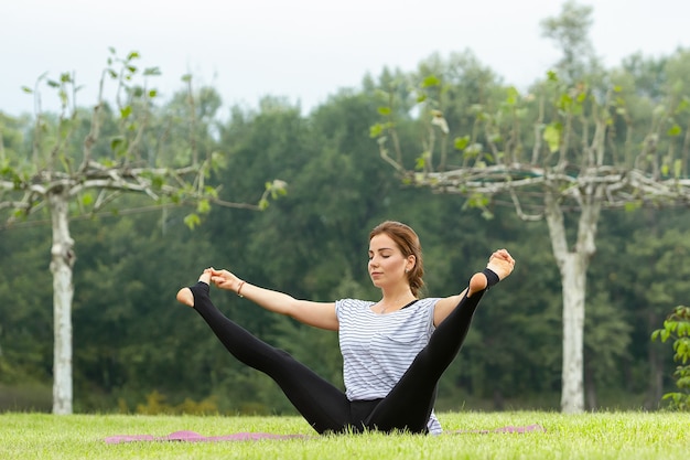 Junge schöne Frau, die Yogaübung im grünen Park tut. Gesundes Lebensstil- und Fitnesskonzept.