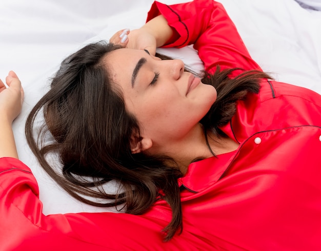 Junge schöne Frau im roten Schlafanzug, der im Bett entspannt