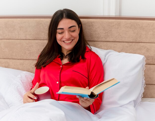 Junge schöne Frau im roten Schlafanzug, der im Bett entspannt