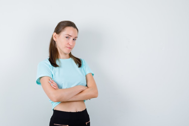 Junge schöne Frau im T-Shirt mit verschränkten Armen und freudlosem Blick, Vorderansicht.