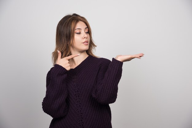 Junge schöne Frau im warmen Strickpullover, der auf ihre Hand zeigt.