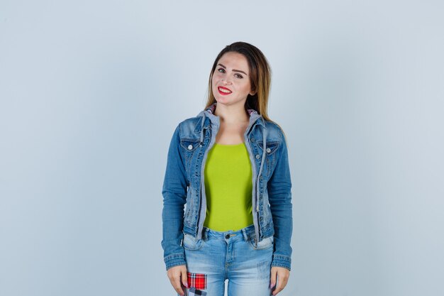 Junge schöne Frau in Denim-Outfit posiert im Stehen und schaut froh, Vorderansicht.