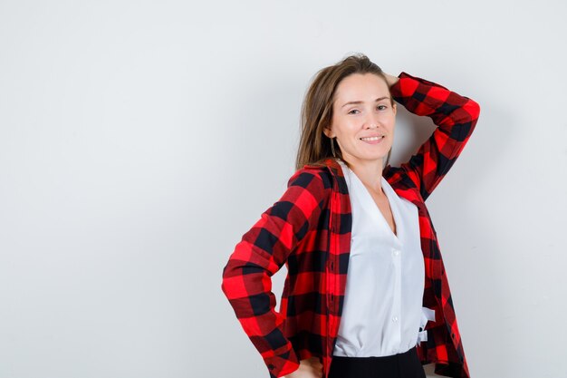 Junge schöne Frau in lässigem Outfit posiert, während sie die Hand hinter dem Kopf hält und fröhlich aussieht, Vorderansicht.