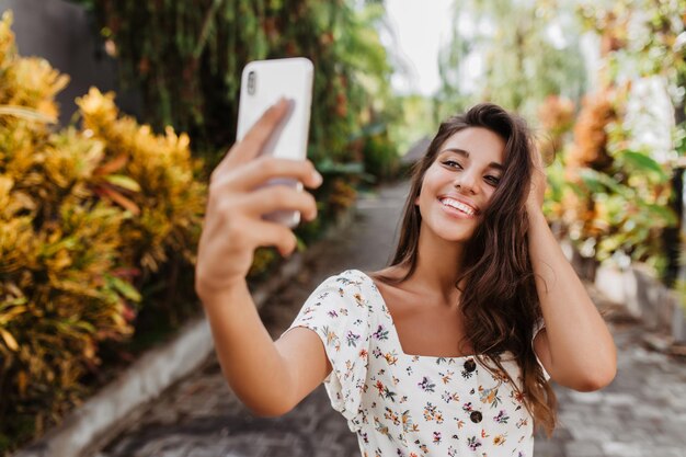 Junge schöne Frau in weißer Sommerbluse mit Lächeln posiert für Selfie im Garten