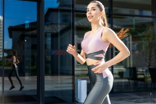 Junge schöne Frau mit einem Pferdeschwanz in einer sportlichen Ausstattung läuft in die Stadt