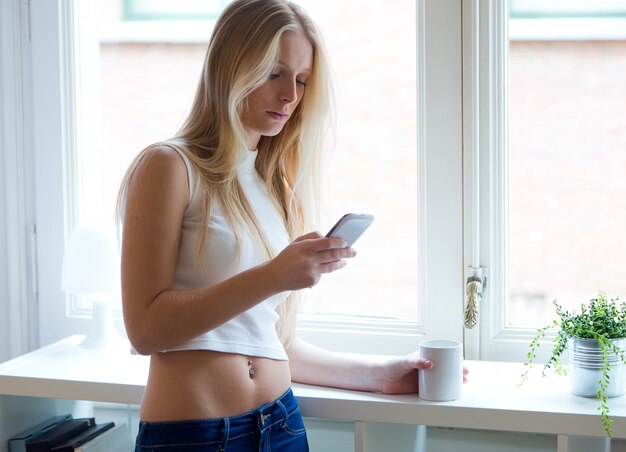 Junge schöne Frau mit ihrem Handy zu Hause.