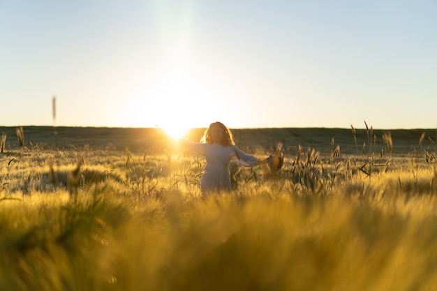 junge schöne Frau mit langen blonden Haaren in einem weißen Kleid auf einem Weizenfeld am frühen Morgen bei Sonnenaufgang. Der Sommer ist die Zeit für Träumer, fliegende Haare, eine Frau, die in den Strahlen über das Feld rennt