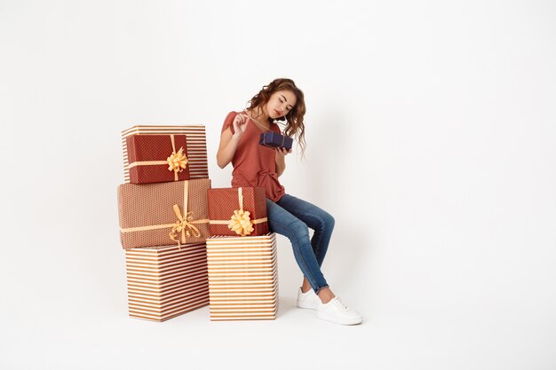 Junge schöne Frau sitzt auf großer Geschenkbox, die kleinere öffnet