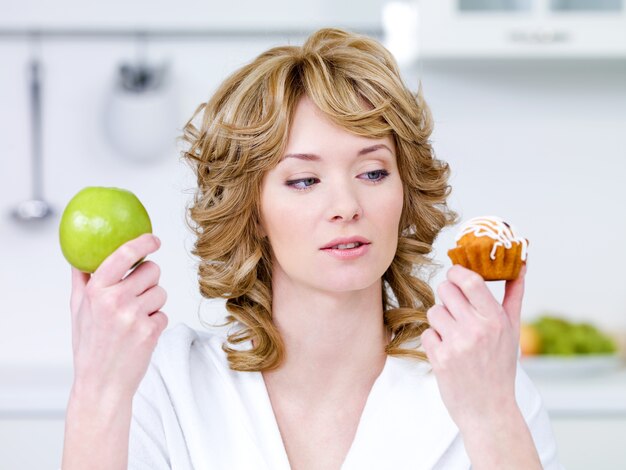 Junge schöne Frau wählen zwischen süßem Kuchen und grünem Apfel