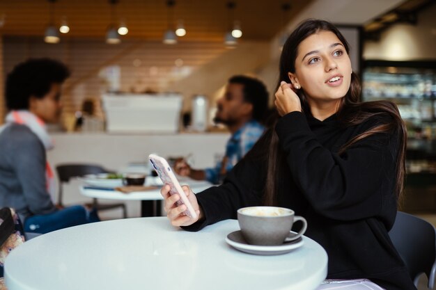 Junge schöne Frauen mit Smartphone, charmante Studentin, die im Café sitzt