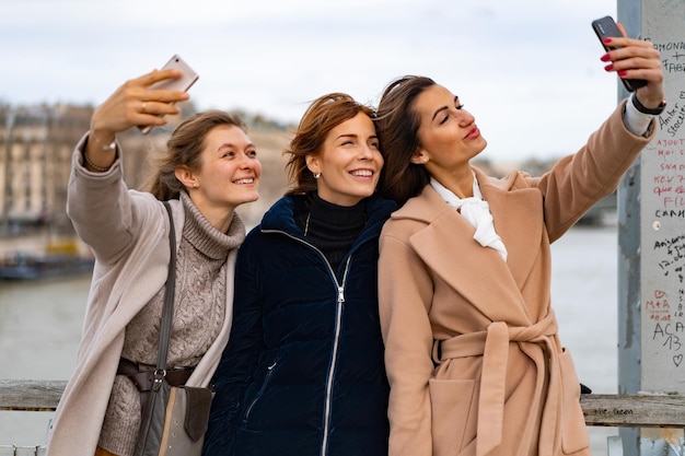 junge schöne freundinnen reisen, machen selfie auf dem smartphone, lachen. Paris. Das Konzept eines glücklichen Reisefotos. Glückliche junge Leute, die Selfies in der Stadt machen