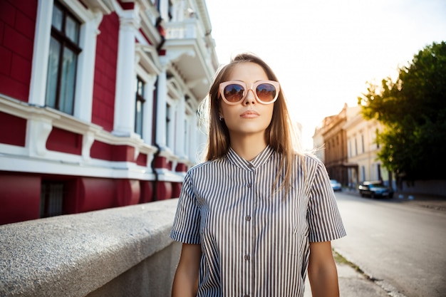 Junge schöne fröhliche Frau in der Sonnenbrille, die durch Stadt geht