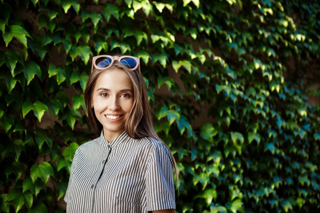 Junge schöne fröhliche Frau in der Sonnenbrille, die um Stadt geht, lächelnd.