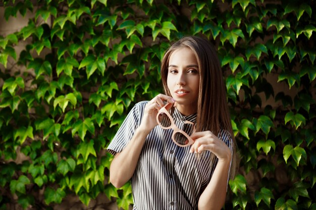 Junge schöne fröhliche Frau in der Sonnenbrille, die um Stadt geht, lächelnd.