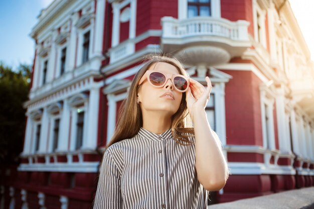 Junge schöne fröhliche Frau in der Sonnenbrille, die um Stadt geht, lächelnd.