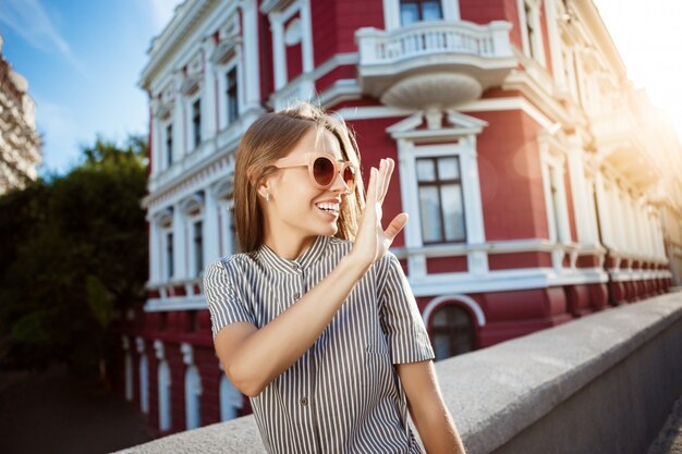 Junge schöne fröhliche Frau in der Sonnenbrille, die um Stadt geht, lächelnd.