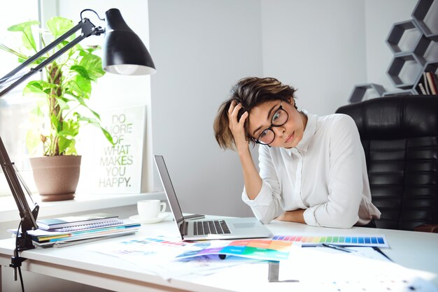 Junge schöne Geschäftsfrau, die am Arbeitsplatz im Büro denkt.