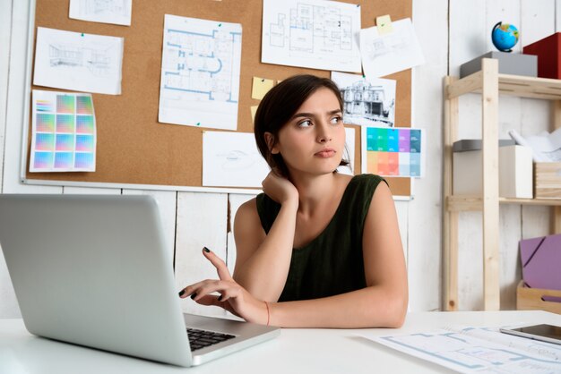 Junge schöne Geschäftsfrau, die am Arbeitsplatz mit Laptop sitzt