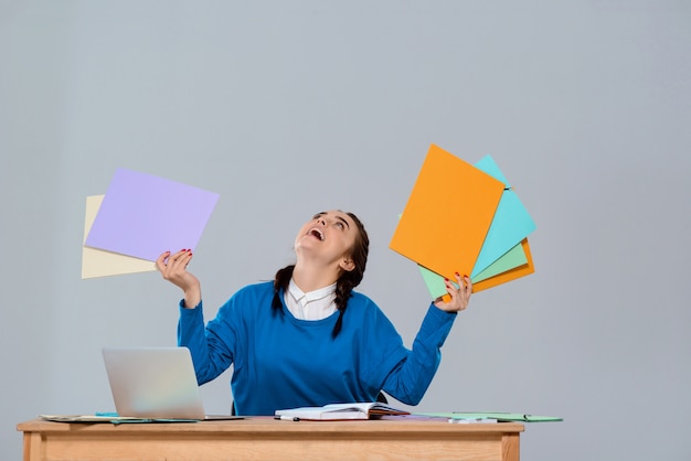 Junge schöne Geschäftsfrau, die am Arbeitsplatz sitzt und bunte Ordner hält