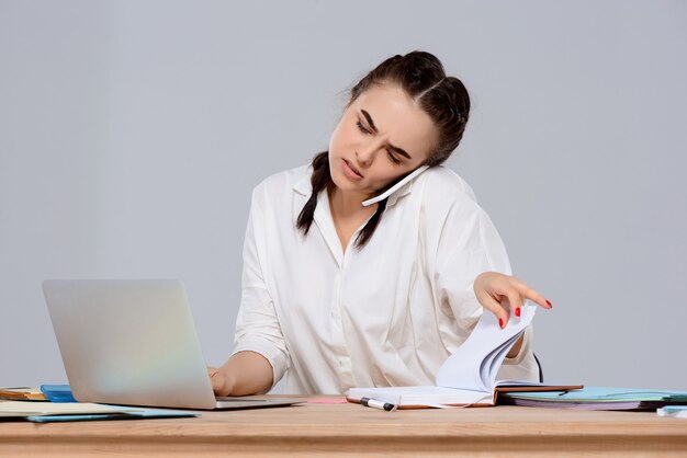 Junge schöne Geschäftsfrau, die am Telefon am Arbeitsplatz spricht