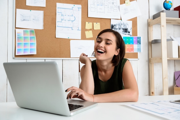 Junge schöne Geschäftsfrau lächelnd, am Arbeitsplatz tippend auf Laptop