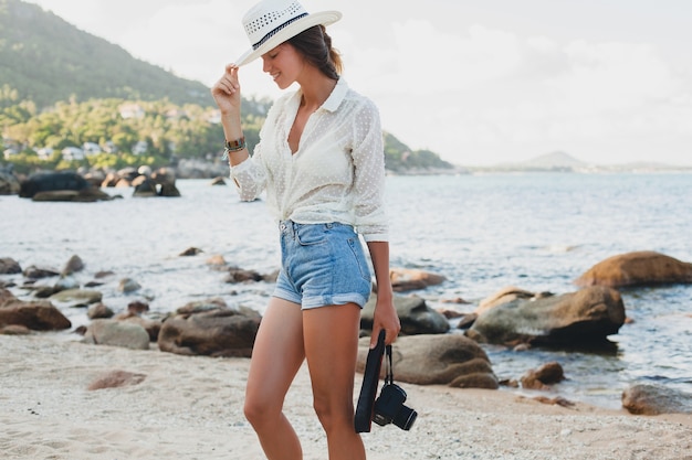Junge schöne Hipster-Frau im Sommerurlaub in Asien, entspannend am tropischen Strand, digitale Fotokamera, lässiger Boho-Stil, Seelandschaft, schlank gebräunter Körper, reisen allein
