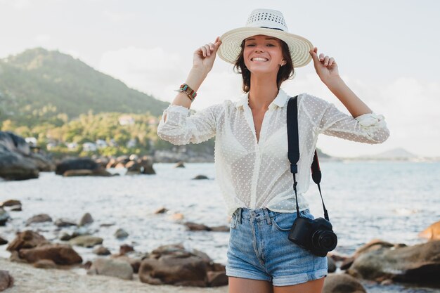 Junge schöne Hipster-Frau im Sommerurlaub in Asien, entspannend am tropischen Strand, digitale Fotokamera, lässiger Boho-Stil, Seelandschaft, schlank gebräunter Körper, reisen allein