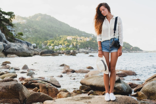 Junge schöne Hipster-Frau im Sommerurlaub in Asien, entspannend am tropischen Strand, digitale Fotokamera, lässiger Boho-Stil, Seelandschaft, schlank gebräunter Körper, reisen allein