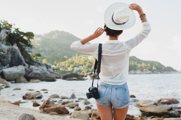 Junge schöne Hipster-Frau in den Sommerferien in Asien, Entspannen am tropischen Strand, digitale Fotokamera, lässiger Boho-Stil, Seelandschaft, schlank gebräunter Körper, Reisen allein, Freiheit