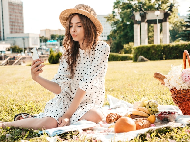 Junge schöne Hipster-Frau in trendigen Sommerjeans, rosa T-Shirt und Hut. Sorglose Frau, die draußen Picknick macht.