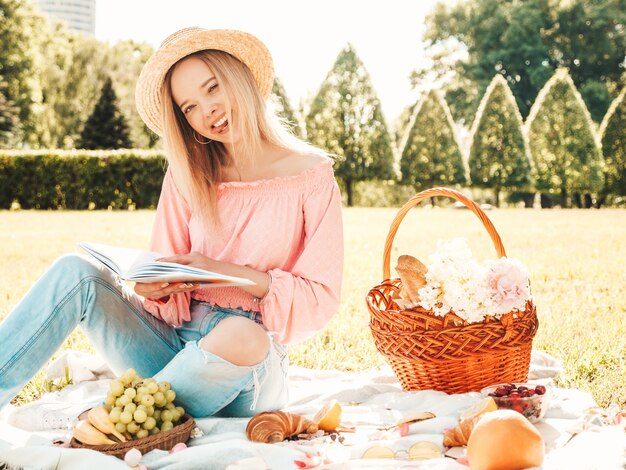 Junge schöne Hipster-Frau in trendigen Sommerjeans, rosa T-Shirt und Hut. Sorglose Frau, die draußen Picknick macht.