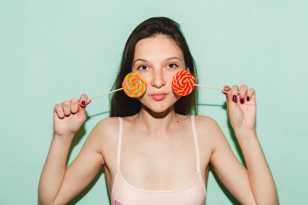 Junge schöne Hipsterfrau, die gegen blaue Wand aufwirft, lolly Popbonbon hält