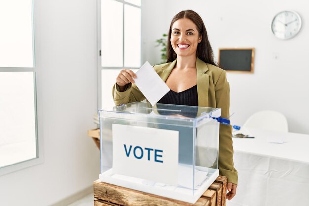 Junge schöne hispanische Frau lächelt selbstbewusst und stimmt an der Wahlurne im Wahlkollegium ab