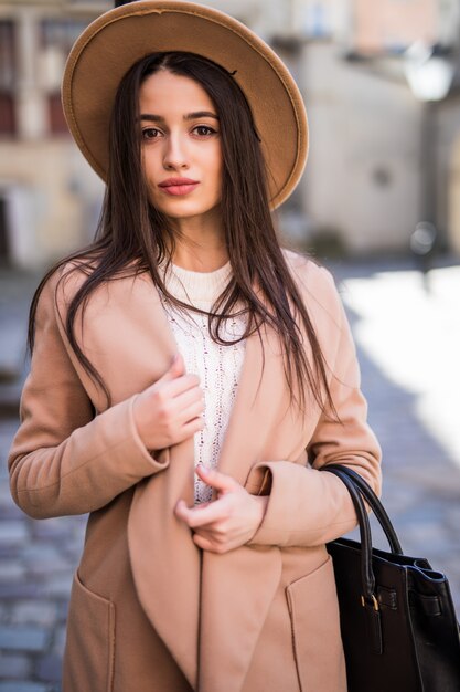 Junge schöne hübsche Frau, die entlang der Straße geht, gekleidet in lässigen Herbstkleidung hellen Mantel
