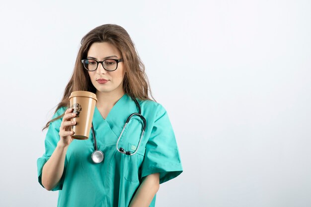 Junge schöne Krankenschwester mit Stethoskop, die eine Tasse Kaffee hält