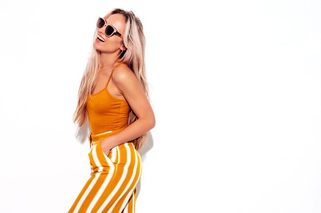 Junge schöne lächelnde blonde Frau in trendiger gelber Sommerkleidung Sexy sorglose Frau isoliert auf weiß im Studio Positives Modell, das Spaß im Innenbereich hat Fröhlich und glücklich In Sonnenbrille