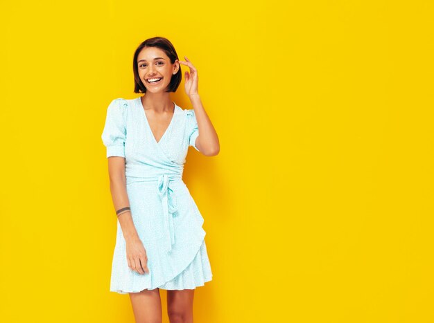 Junge schöne lächelnde Frau im trendigen blauen Sommerkleid Sexy sorglose Frau posiert in der Nähe der gelben Wand im Studio Positives Modell, das Spaß hat Fröhlich und glücklich Isoliert