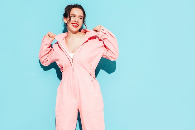 Junge schöne lächelnde Frau im trendigen rosafarbenen Sommeroverall Sexy sorglose Frau posiert in der Nähe der blauen Wand im Studio mit zwei Hörnern Positives Modell, das Spaß hat und verrückt wird Fröhlich und glücklich