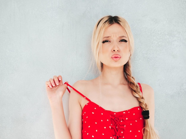 Junge schöne lächelnde Frau im trendigen roten Sommerkleid Sexy sorglose blonde Frau posiert in der Nähe der Wand im Studio Positives Modell, das Spaß hat Fröhlich und glücklich Am sonnigen Tag