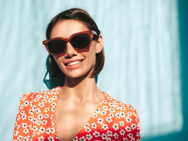 Junge schöne lächelnde Frau im trendigen roten Sommerkleid Sexy sorglose Frau posiert in der Nähe der blauen Wand im Studio Positives Modell, das Spaß hat Fröhlich und glücklich Am sonnigen Tag Schatten vom Fenster