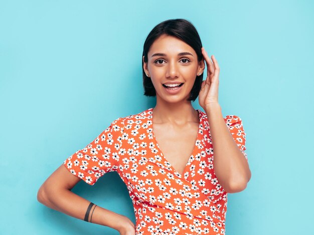 Junge schöne lächelnde Frau im trendigen roten Sommerkleid Sexy sorglose Frau posiert in der Nähe der blauen Wand im Studio Positives Modell, das Spaß hat Fröhlich und glücklich Isoliert