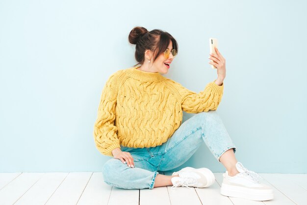 Junge schöne lächelnde Frau in trendigem, gelbem Hipster-Pullover und Jeans