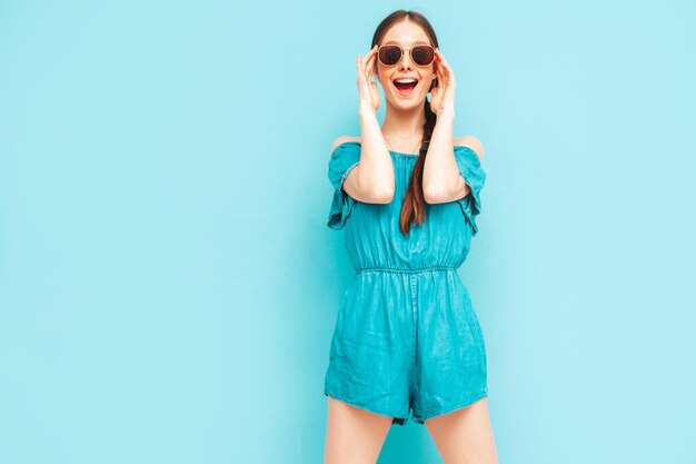 Junge schöne lächelnde Frau in trendigen Sommerjeans Overalls Sexy sorglose Frau mit Schwanzfrisur posiert in der Nähe der Wand im Studio Positives Modell, das Spaß hat Fröhlich und glücklich Isoliert